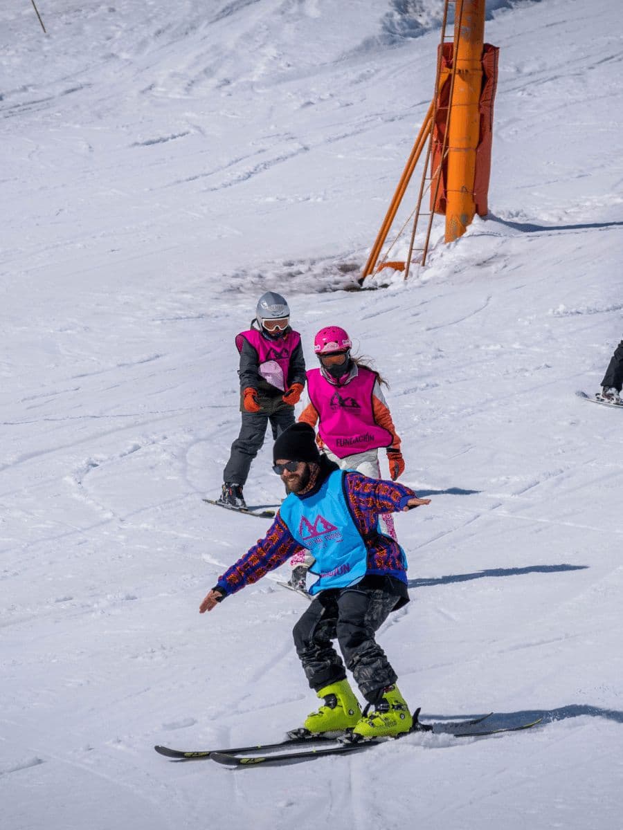 Voluntario enseñando a esquiar a dos estudiantes en la nieve